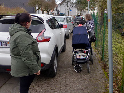 Ein parkendes Auto macht den Gehweg sehr eng. Kinderwagen und Fußgängerin kommen nicht aneinander vorbei.er